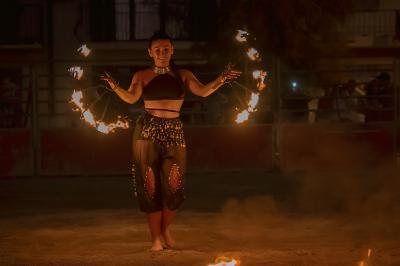 Une femme jongle avec des anneaux enflammés lors d'une performance nocturne en extérieur.