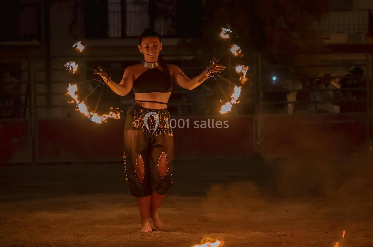 Une femme jongle avec des anneaux enflammés lors d'une performance nocturne en extérieur.