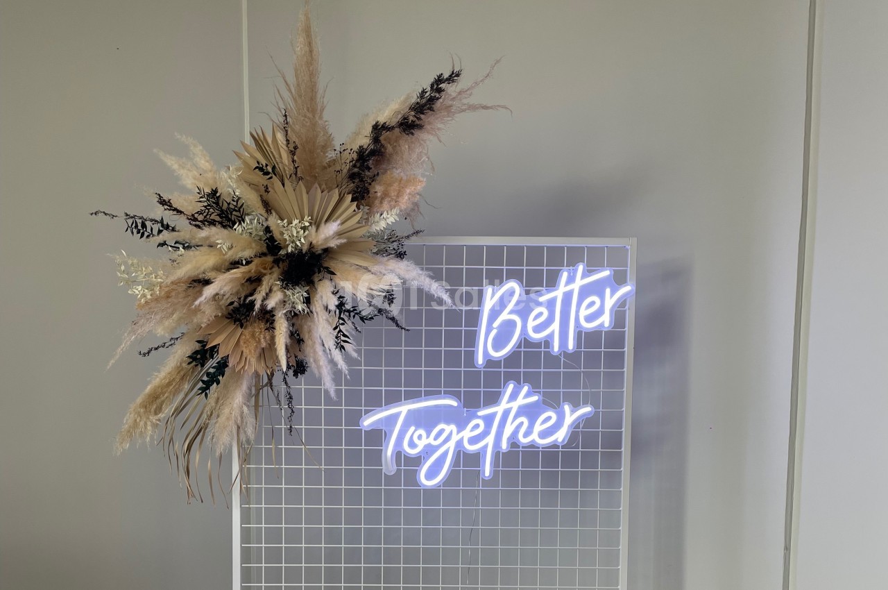 Panneau lumineux ’Better Together’ sur une grille blanche, décoré de fleurs séchées dans des tons neutres.