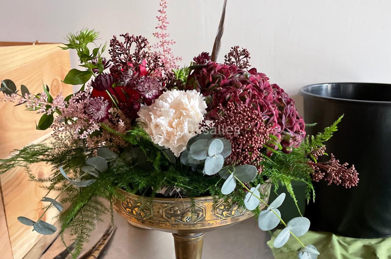 Composition florale dans une coupe en métal doré, avec des fleurs rouges, blanches et feuillages verts.