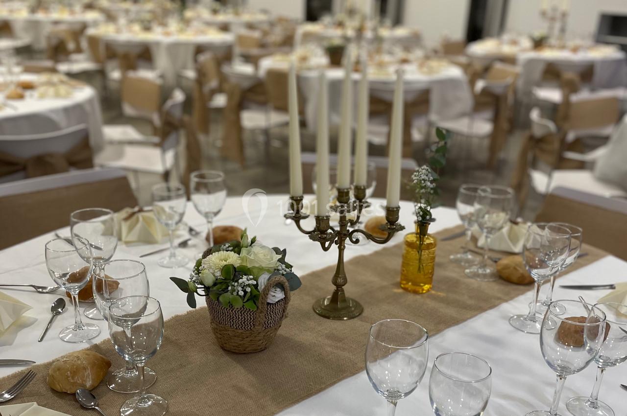 Table décorée pour un événement avec chandelier, fleurs, nappes blanches et vaisselle disposée élégamment.