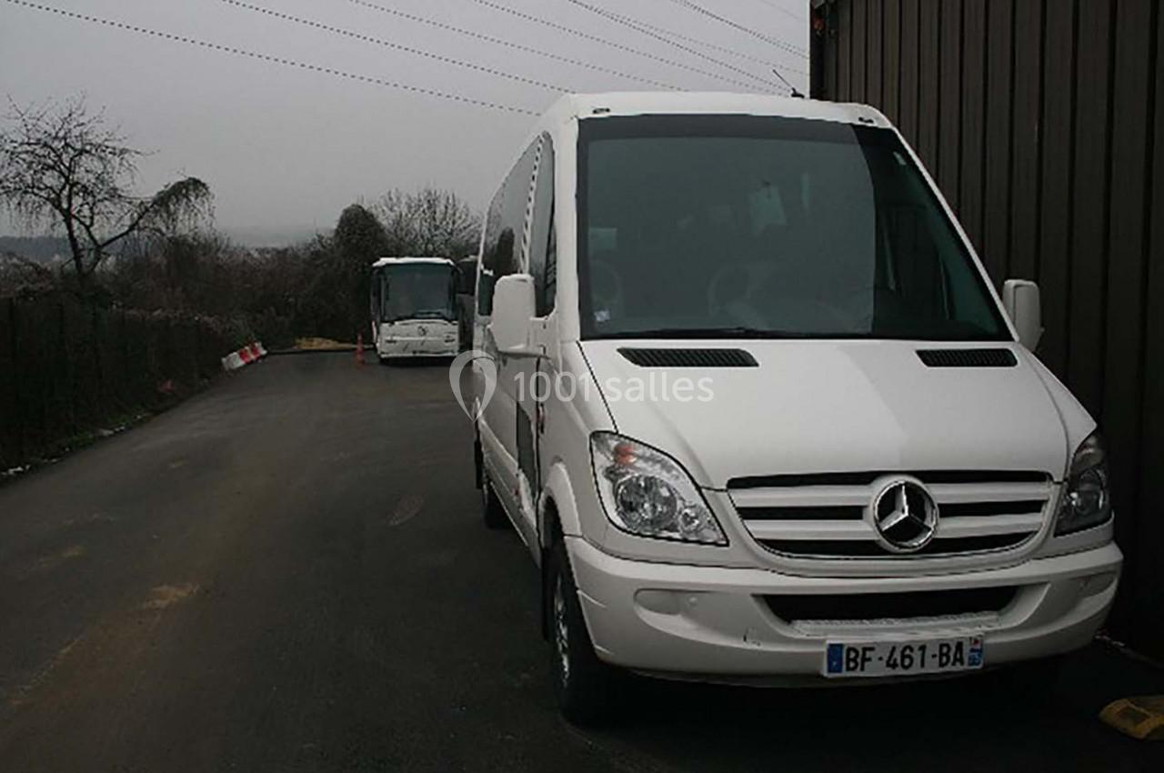 Deux minibus blancs stationnés sur une route asphaltée par temps couvert, avec des arbres en arrière-plan.