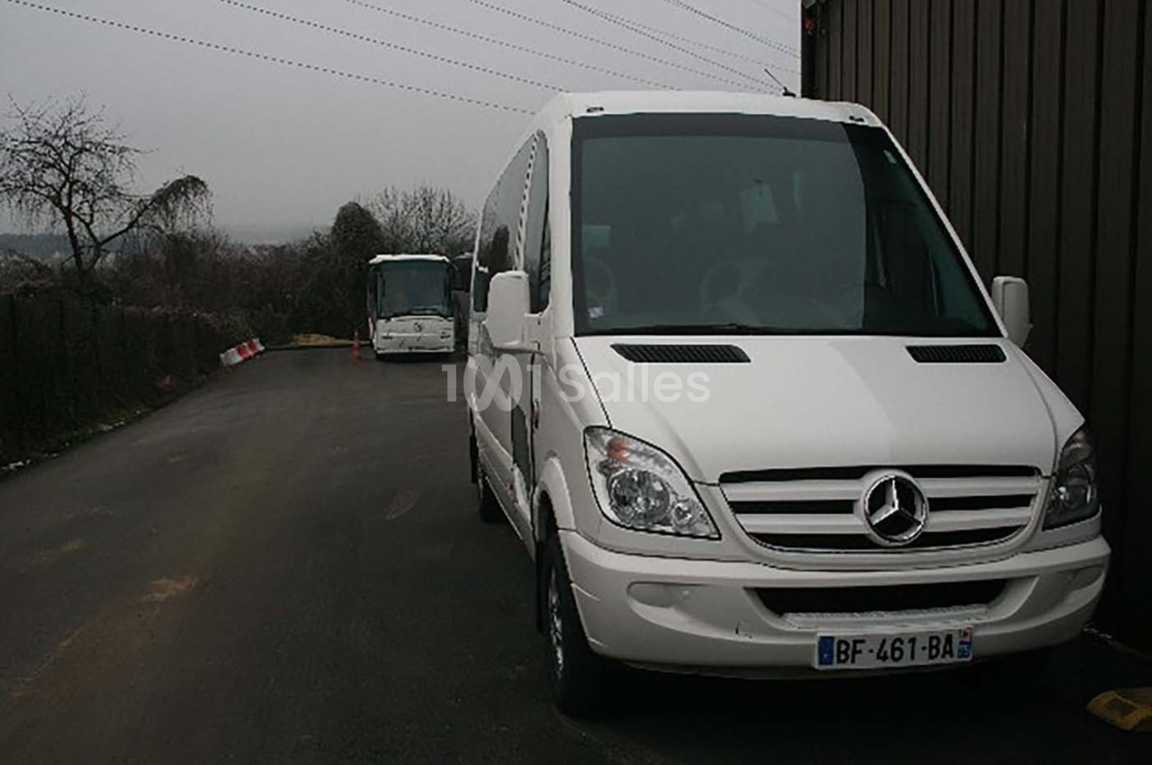 Deux minibus blancs stationnés sur une route asphaltée par temps couvert, avec des arbres en arrière-plan.