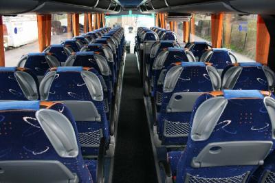 Vue intérieure d'un autocar avec des sièges rembourrés et un toit vitré laissant passer la lumière naturelle.