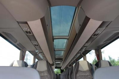 Vue intérieure d'un autocar avec des sièges rembourrés et un toit vitré laissant passer la lumière naturelle.