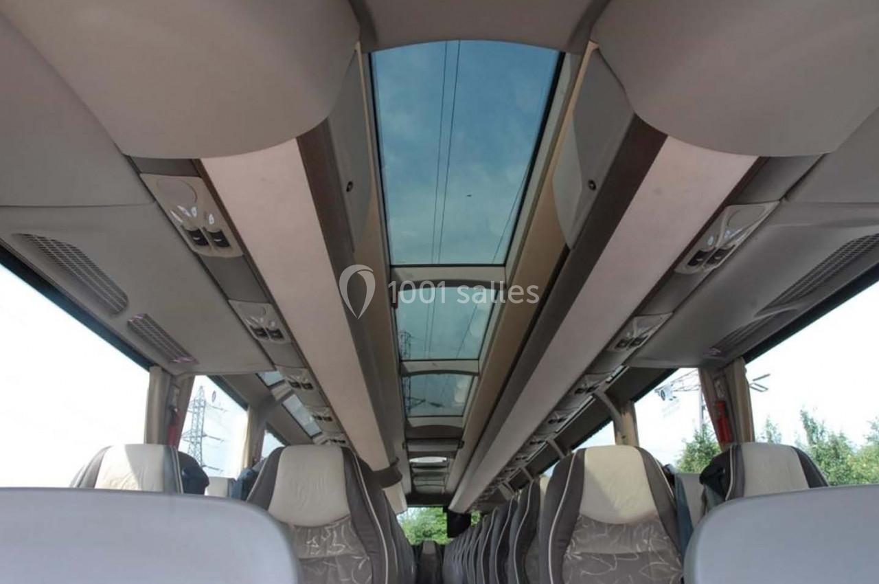 Vue intérieure d'un autocar avec des sièges rembourrés et un toit vitré laissant passer la lumière naturelle.