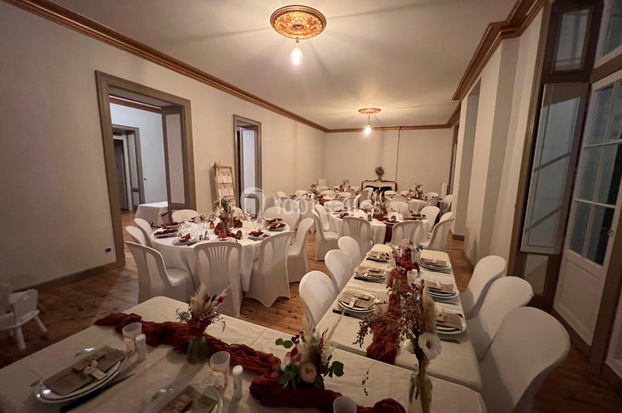 Salle de réception décorée avec des tables dressées, nappes blanches, chaises assorties et ornements floraux rouges.