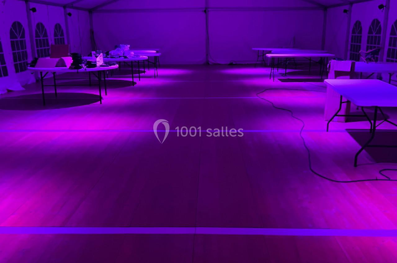 Intérieur d'une grande tente éclairée par une lumière violette, avec des tables disposées et des câbles au sol.