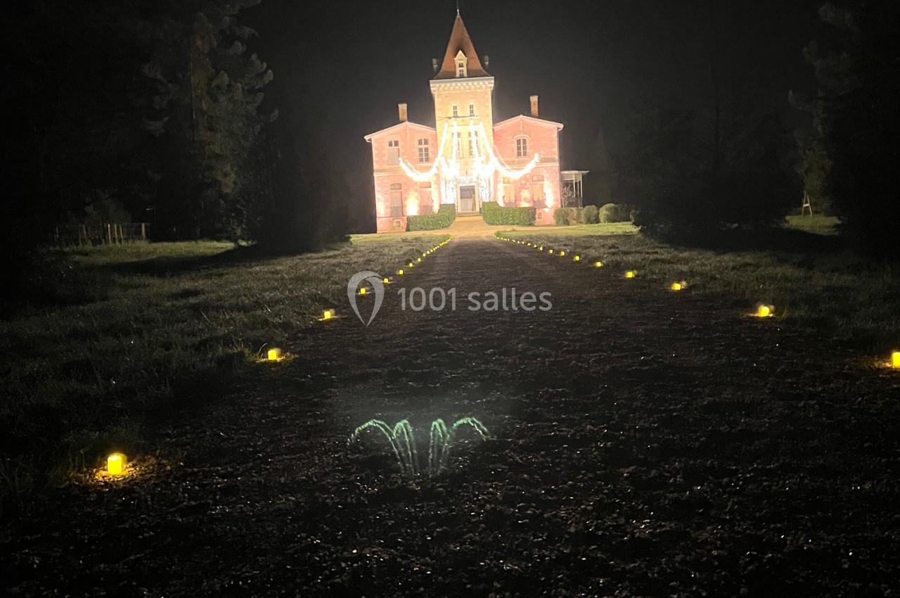 Château illuminé de nuit avec une allée bordée de petites lumières au sol, entouré de végétation sombre.