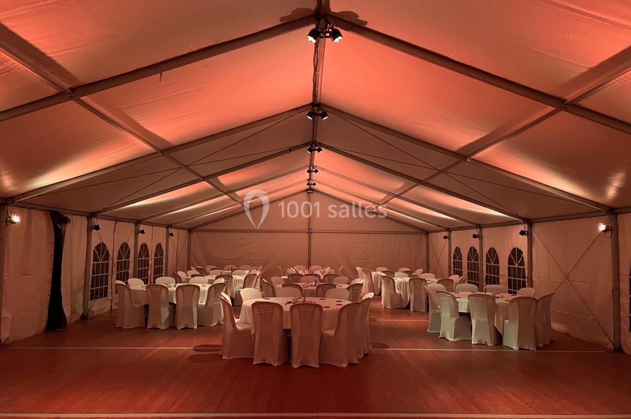 Intérieur d'une tente éclairée en rouge, avec des tables rondes et des chaises blanches disposées pour un événement.