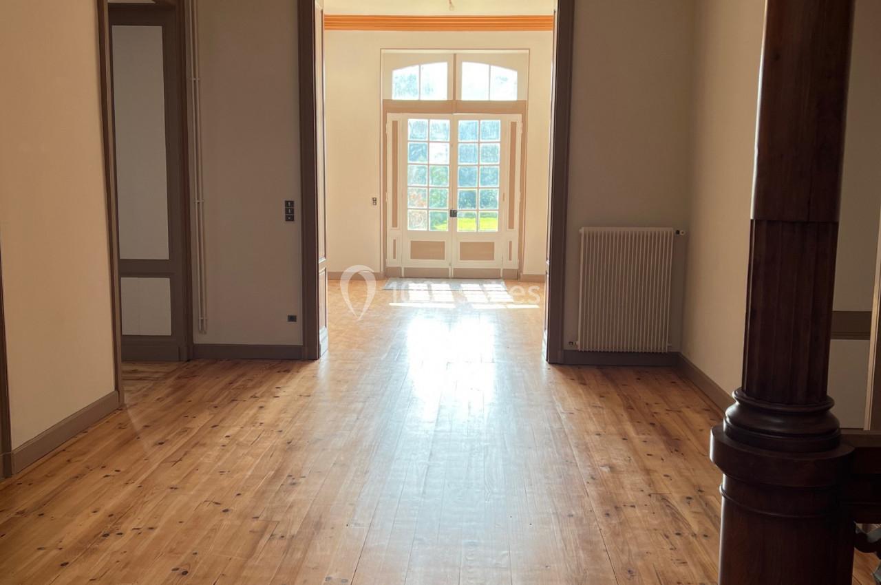 Couloir lumineux avec parquet en bois, ouvert sur une porte vitrée donnant sur un espace extérieur ensoleillé.