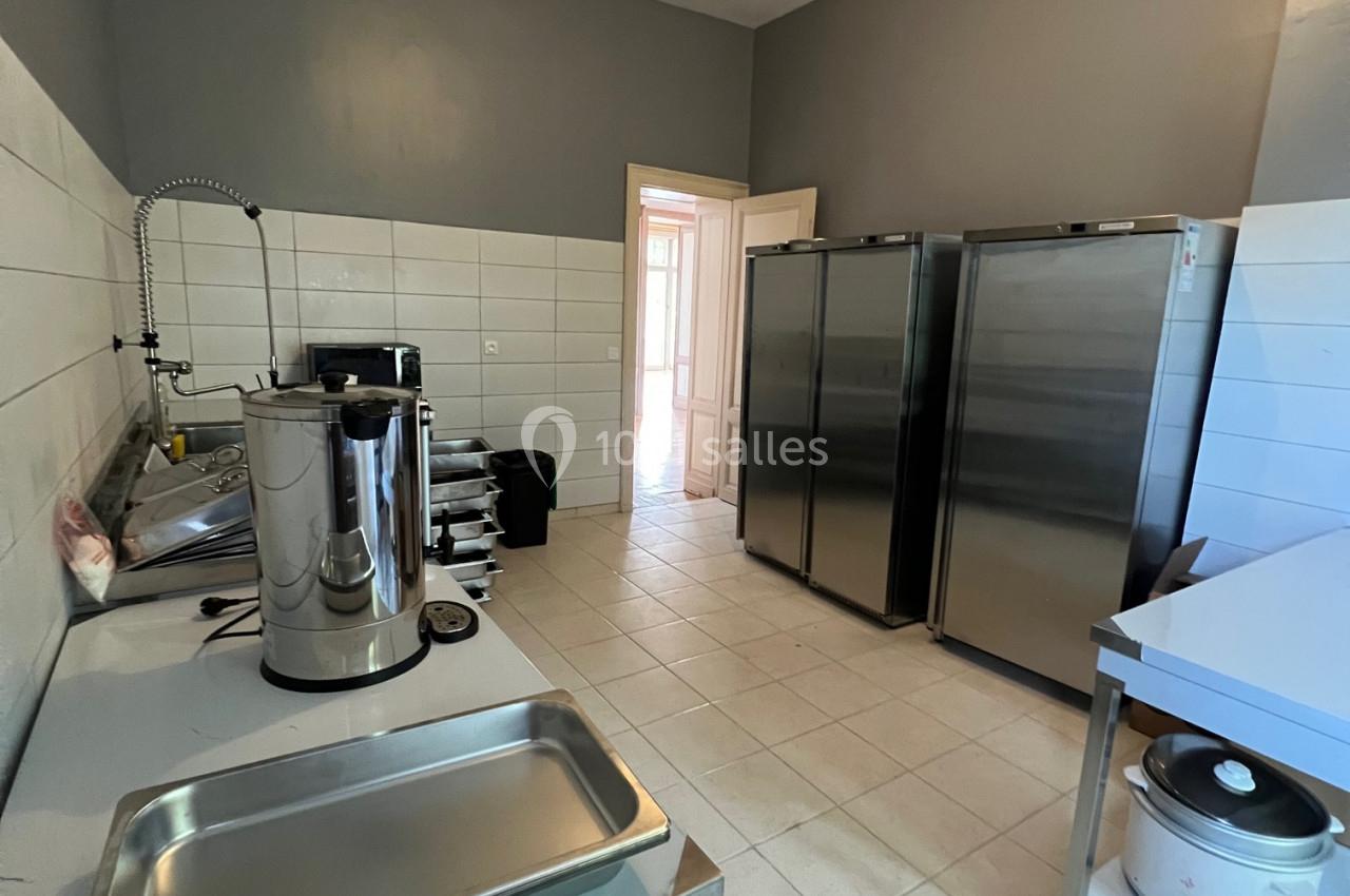 Cuisine professionnelle avec équipements en inox, réfrigérateurs, plans de travail et carrelage clair au sol et aux murs.