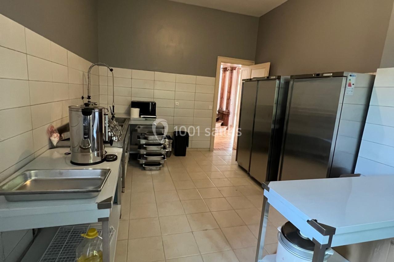 Cuisine professionnelle avec carrelage clair, équipements en inox, plan de travail, évier et réfrigérateurs alignés.