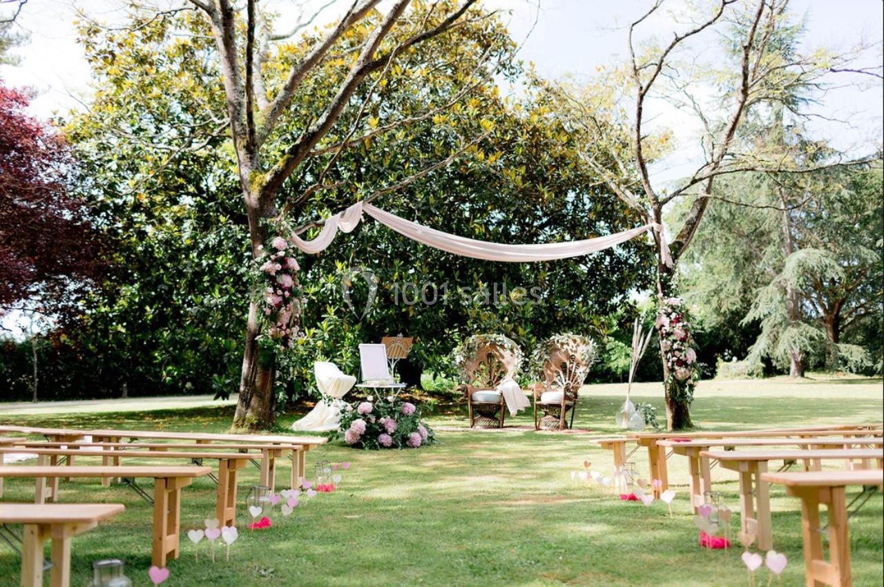 Décoration de cérémonie en plein air avec arche florale, bancs en bois et chaises ornées sous des arbres.