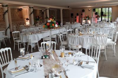 Salle de réception sous une tente avec tables dressées, décorations florales et éclairage suspendu.