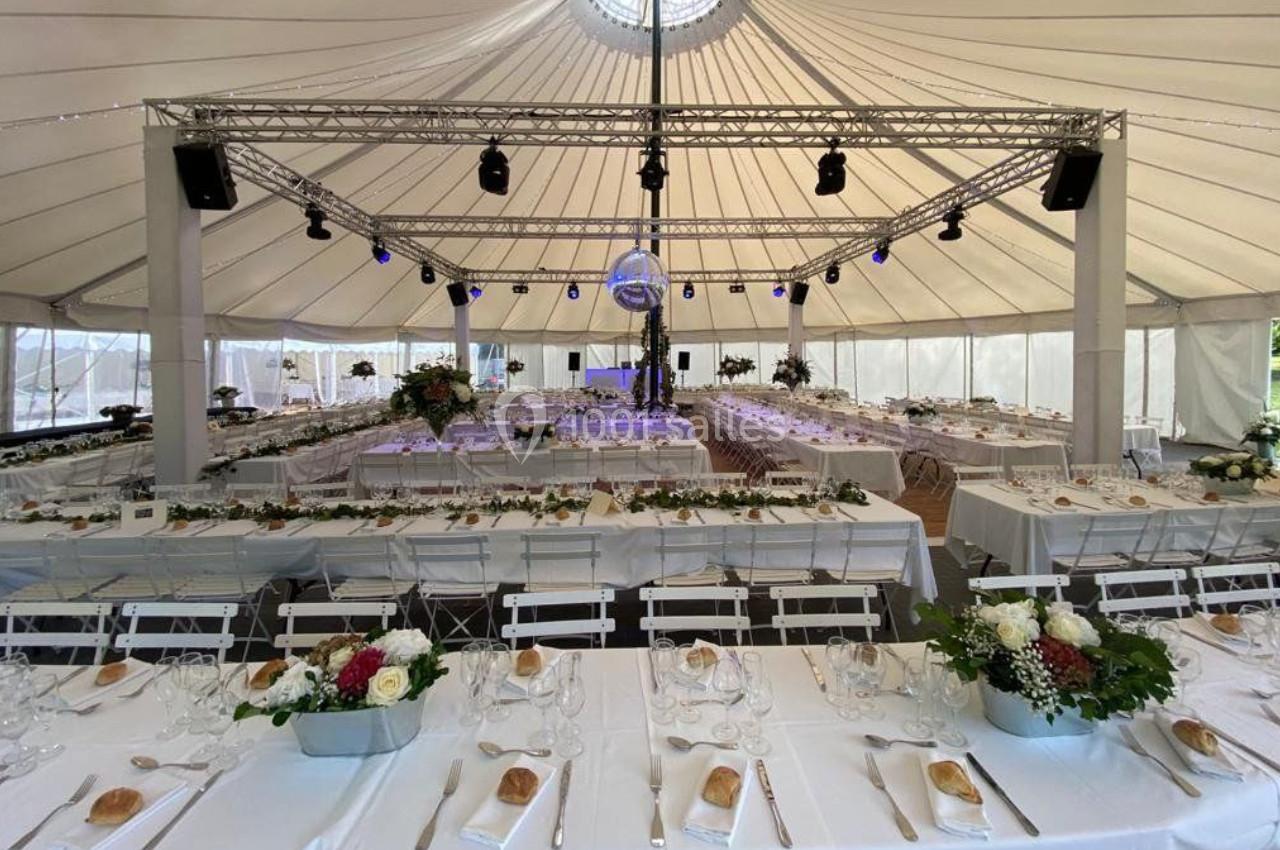 Salle de réception sous une tente avec tables dressées, décorations florales et éclairage suspendu.
