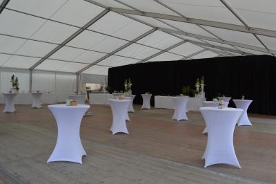 Salle de réception sous une tente avec tables dressées, décorations florales et éclairage suspendu.