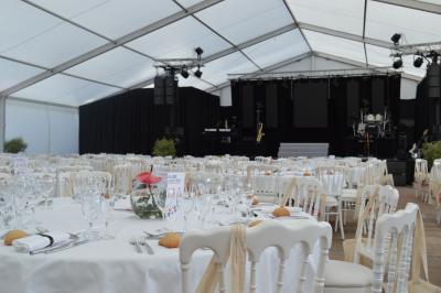 Salle de réception sous une tente avec tables dressées, décorations florales et éclairage suspendu.