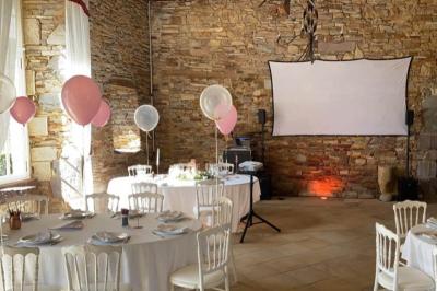 Salle de réception lumineuse avec tables rondes dressées, chaises blanches et décorations florales.