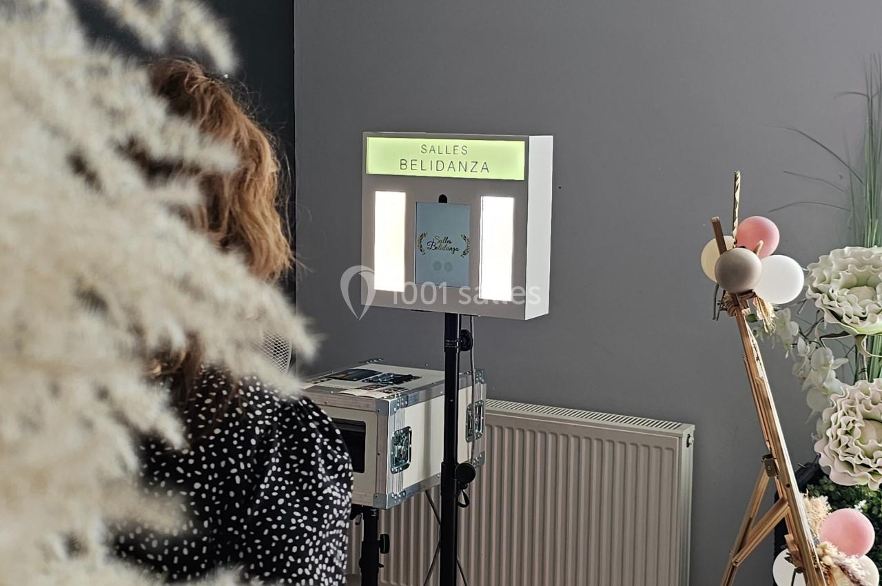 Une femme assise devant une borne photo dans une salle décorée avec des fleurs et des ballons.