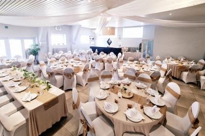 Miniature Location salle Charleroi (Hainaut) - Salles Belidanza #2 Salle de réception décorée avec des tables rondes, nappes beige, chaises ornées de nœuds et compositions florales.