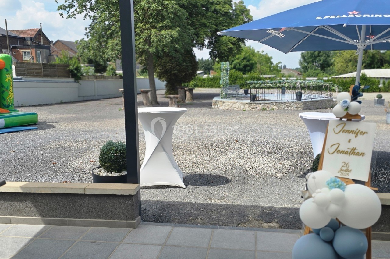 Vue d'une terrasse donnant sur une cour avec une structure gonflable, des tables hautes et une décoration de ballons.
