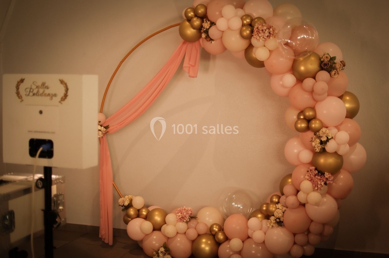 Cercle décoratif en ballons roses, dorés et blancs avec fleurs, installé dans une salle pour un événement.