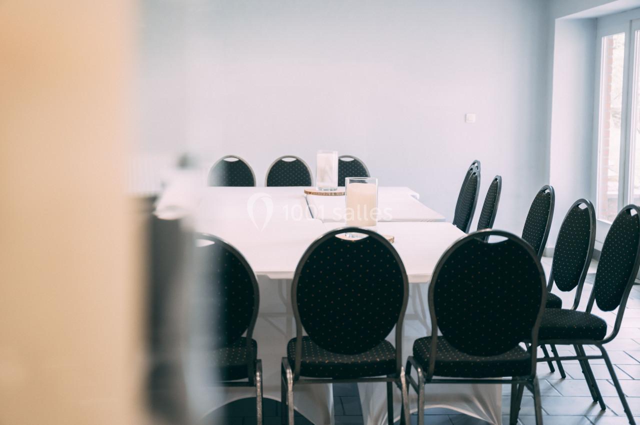 Salle de réunion avec une table rectangulaire recouverte d'une nappe blanche et entourée de chaises noires.