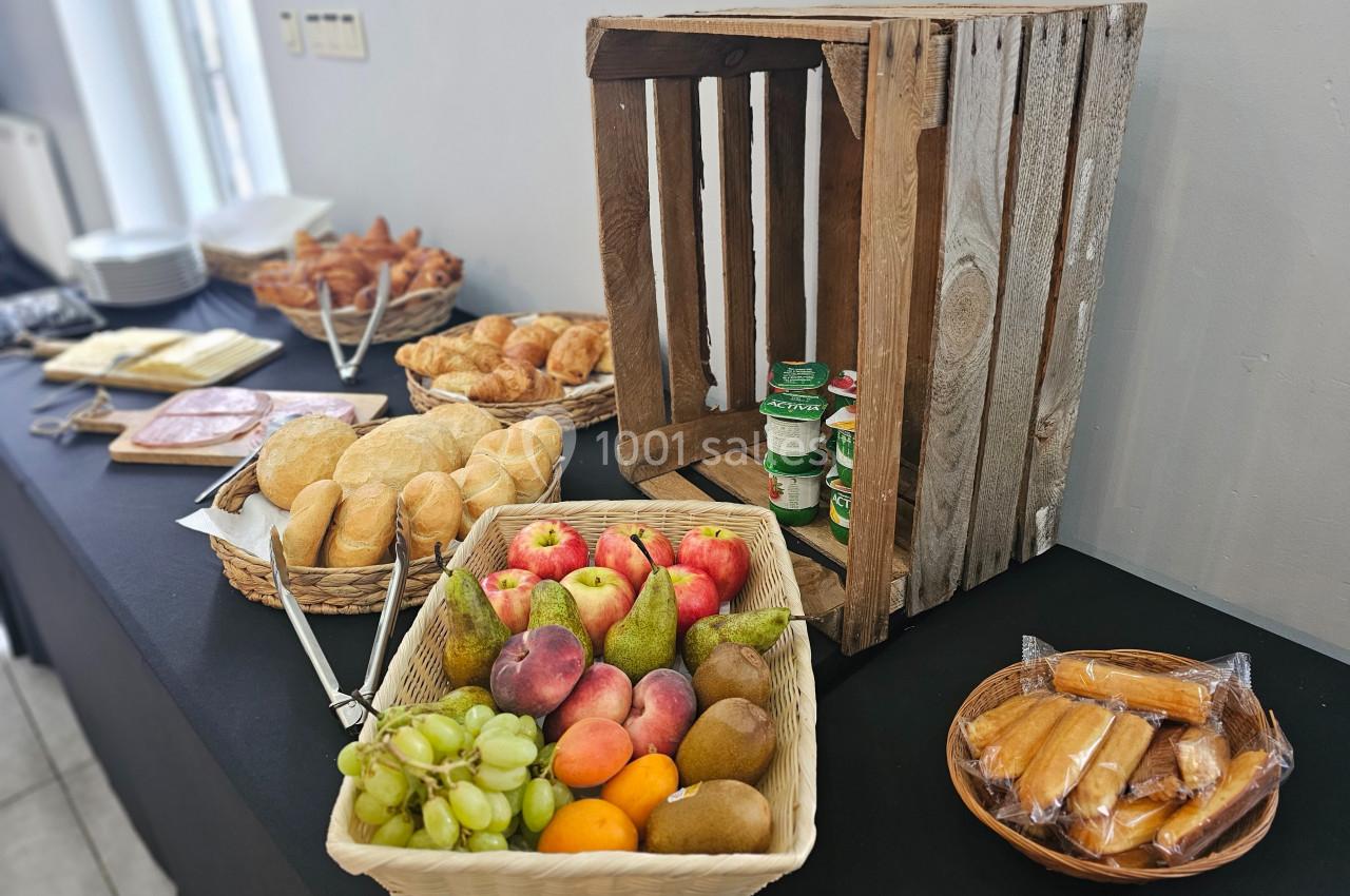 Buffet avec paniers de fruits, viennoiseries, pains, charcuterie, fromages et pots de confiture sur une table noire.