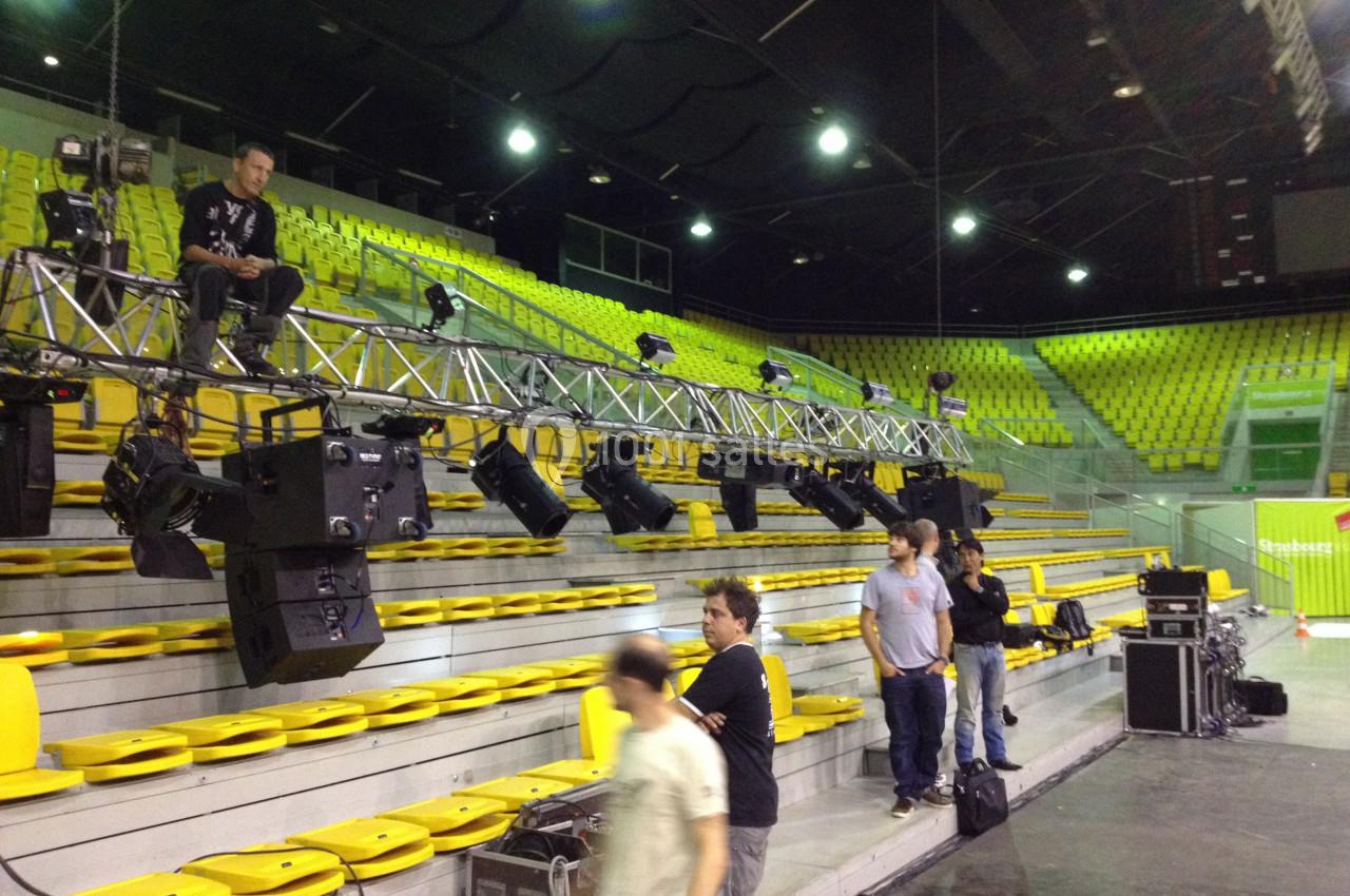 Installation d'un éclairage scénique sur une structure métallique dans des gradins vides d'une salle de spectacle.