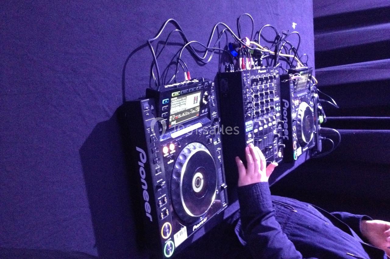 Un DJ manipule une table de mixage et des platines Pioneer sur une surface noire.
