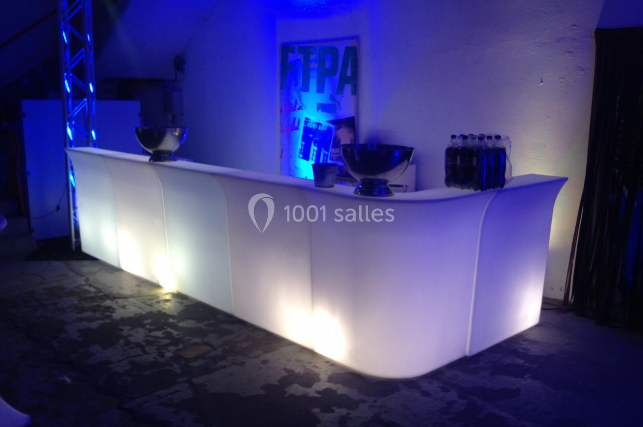 Comptoir lumineux blanc avec bols en métal et bouteilles, éclairé par des lumières bleues dans un espace intérieur sombre.