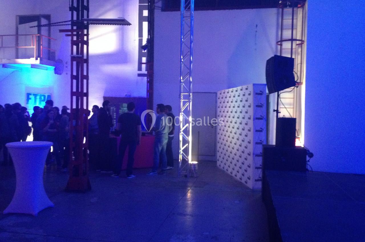 Un événement en intérieur avec des personnes rassemblées près d'un bar éclairé, dans un espace industriel.