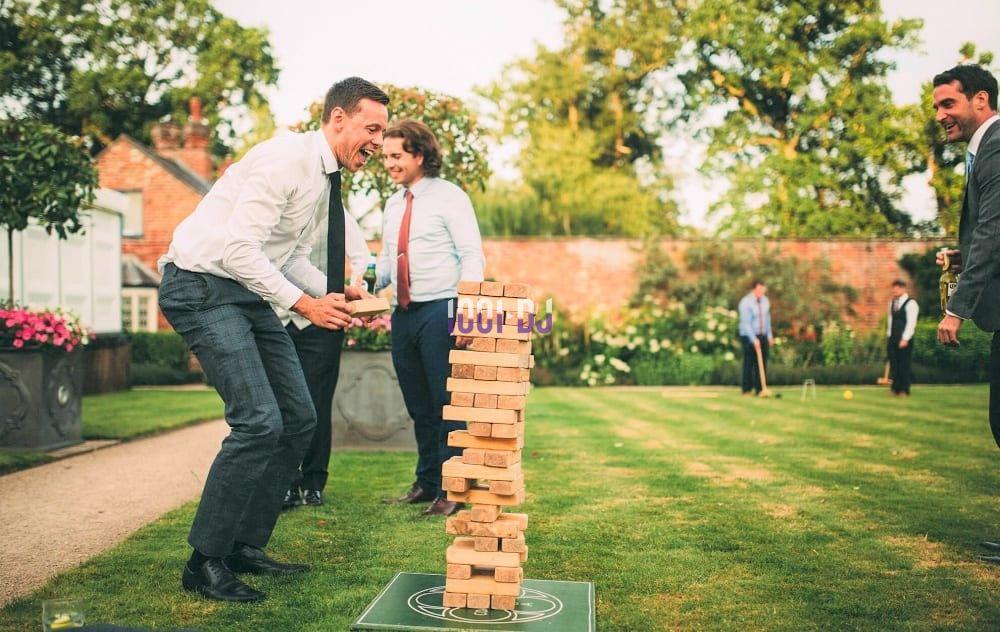 Un groupe de personnes joue à un jeu de blocs en bois dans un jardin lors d'un événement en plein air.