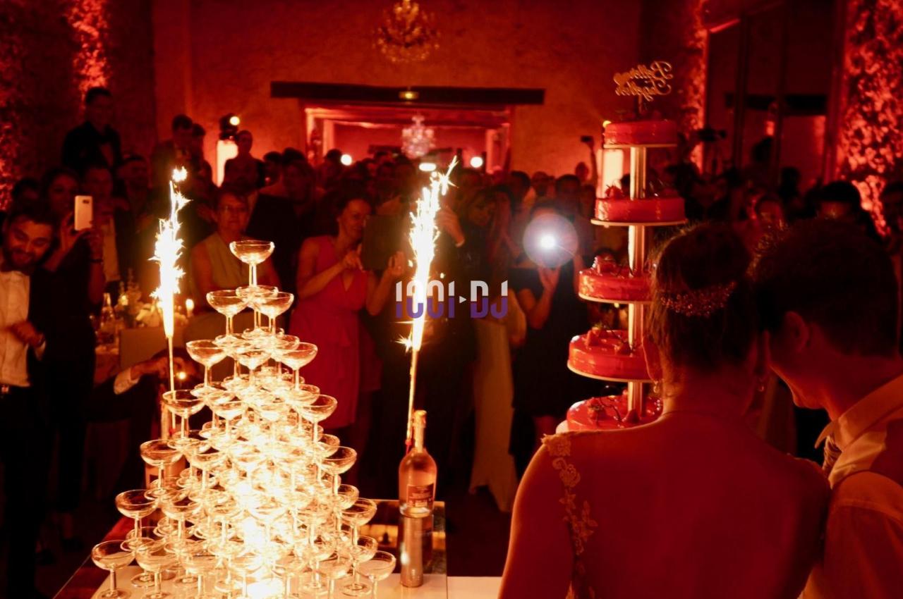 Un couple de mariés observe une fontaine de champagne et un gâteau illuminés par des cierges dans une salle festive.