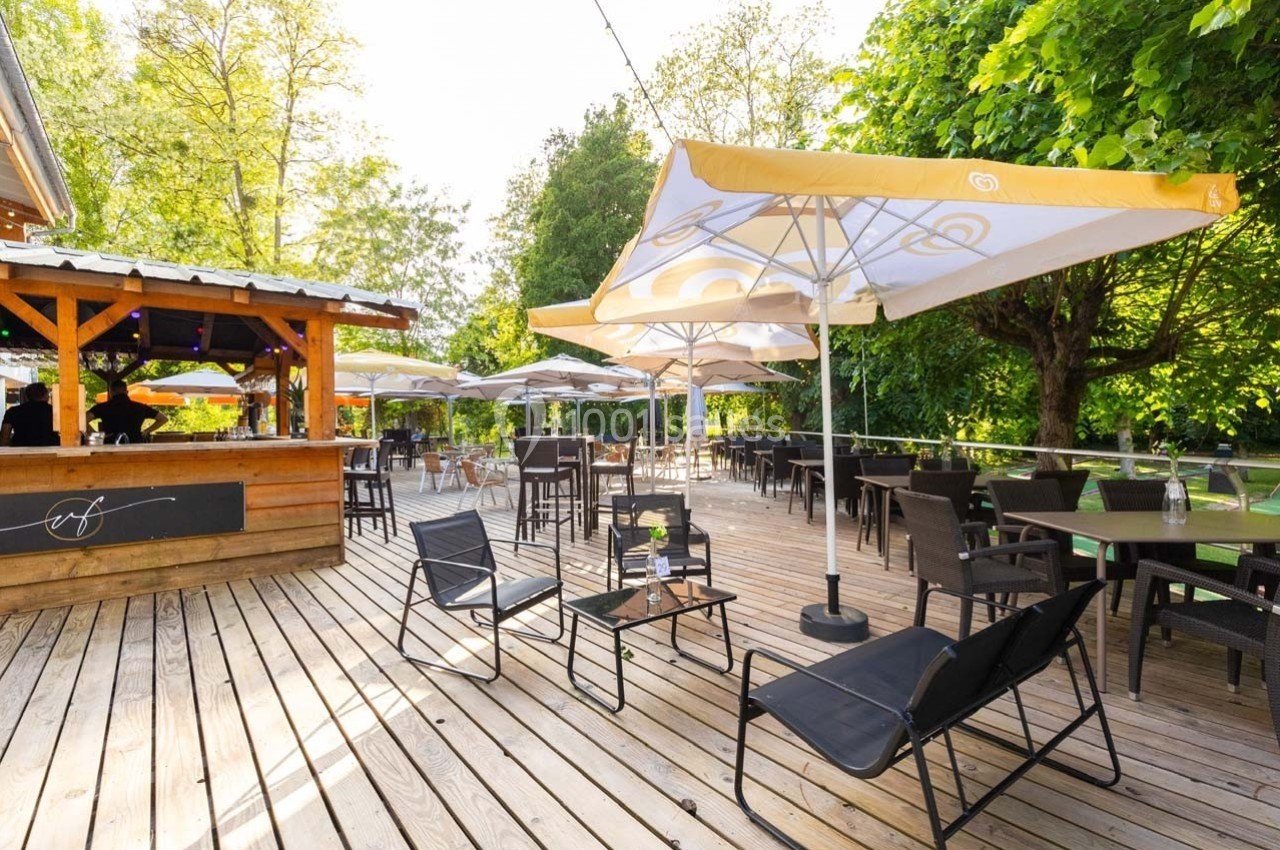 Terrasse en bois avec tables, chaises et parasols jaunes, entourée de verdure sous un ciel dégagé.