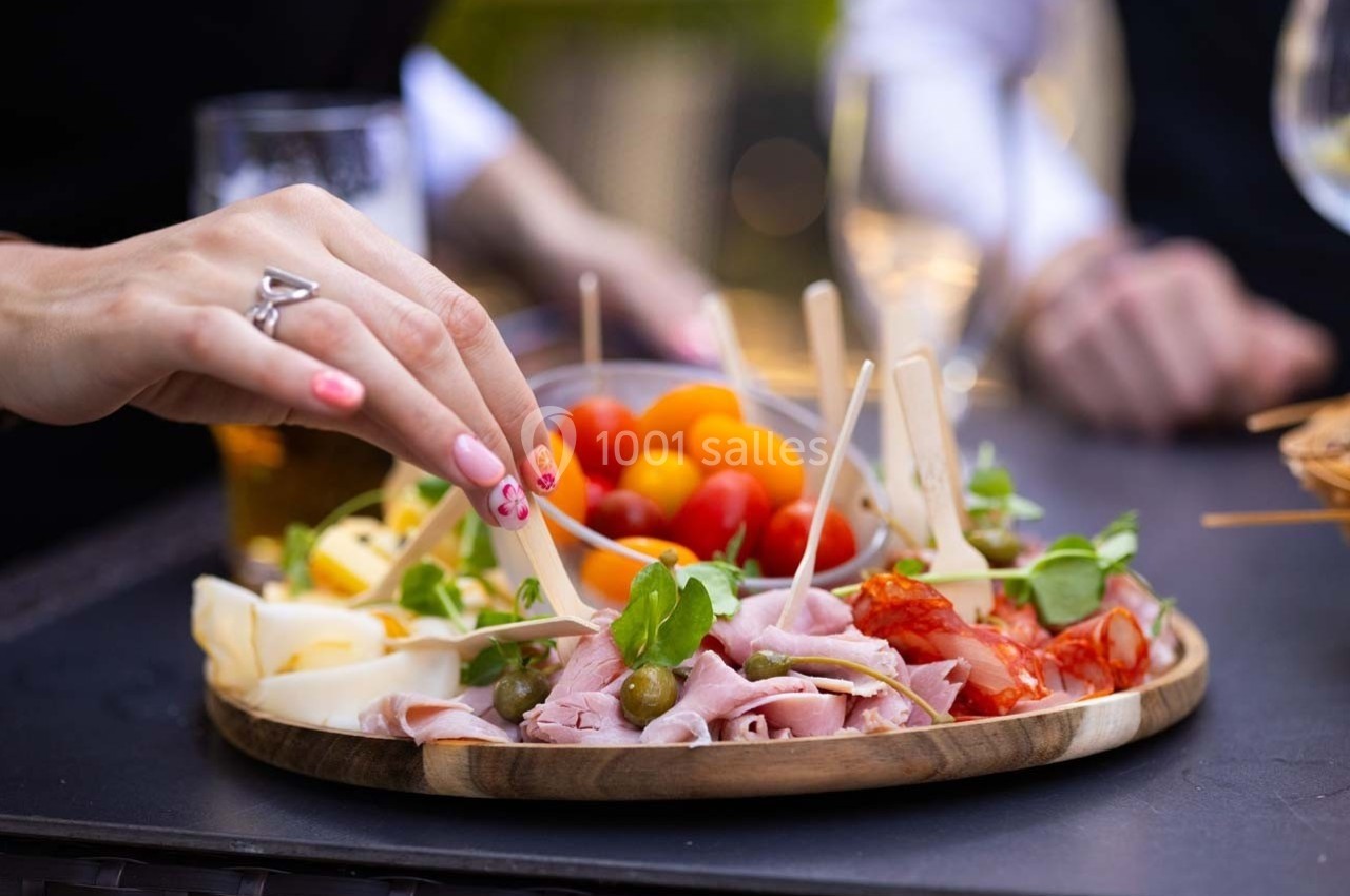 Plateau de charcuterie et fromages avec tomates cerises, olives et herbes, une main prenant un aliment avec un pique.