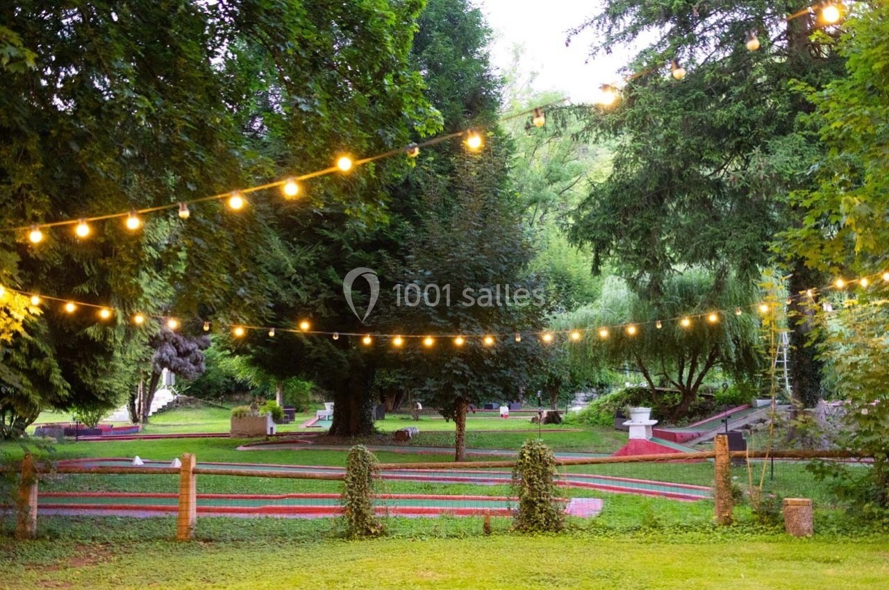 Terrain de mini-golf en plein air entouré d'arbres, éclairé par des guirlandes lumineuses suspendues.