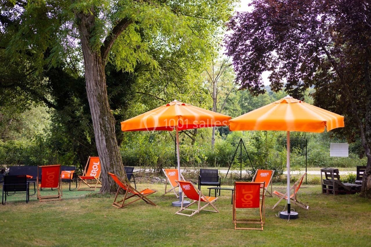 Chaises longues et parasols orange installés sur une pelouse ombragée près d'arbres et d'une clôture.