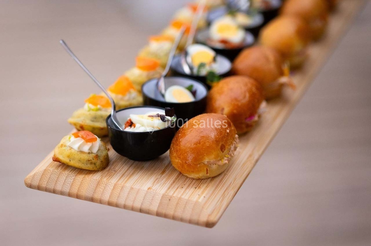 Plateau en bois avec un assortiment de bouchées salées, incluant verrines, mini-sandwichs et amuse-bouches variés.