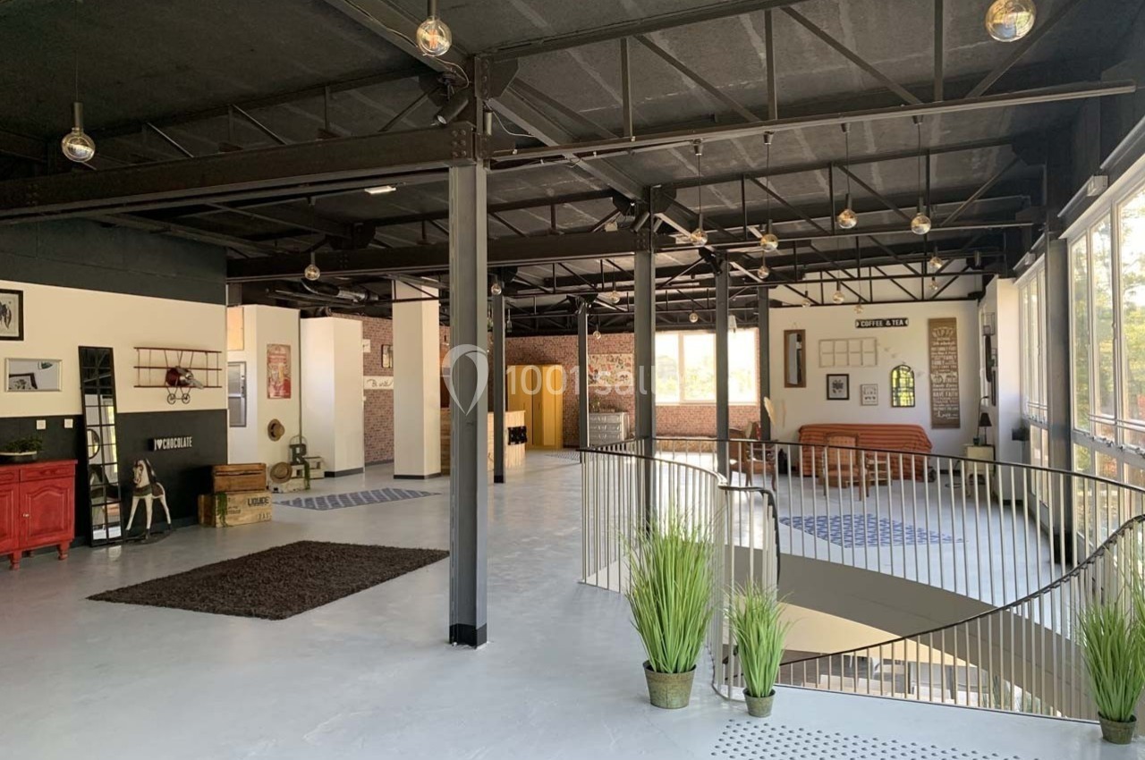Intérieur spacieux et lumineux d'un loft industriel avec mezzanine, grandes fenêtres et décoration moderne.