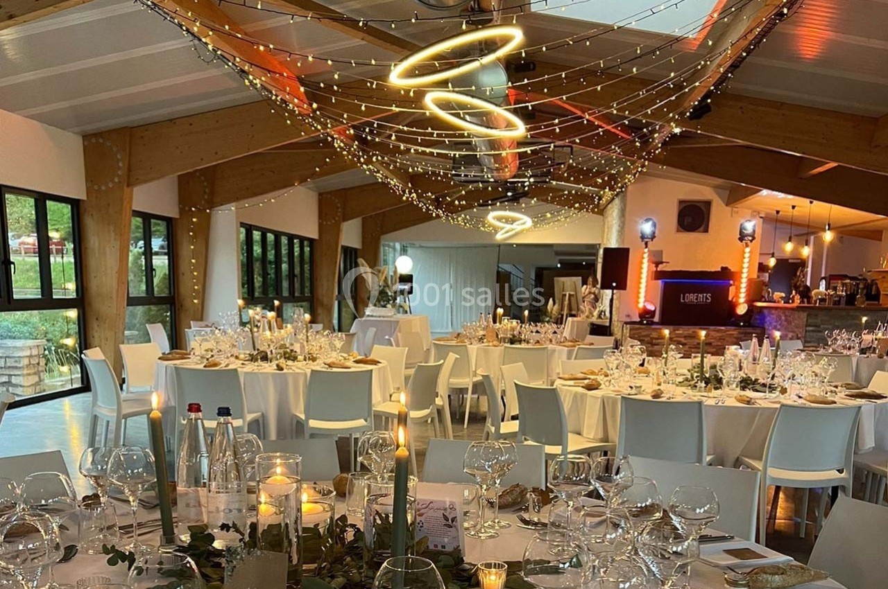 Salle de réception décorée avec des tables dressées, guirlandes lumineuses suspendues et ambiance chaleureuse.