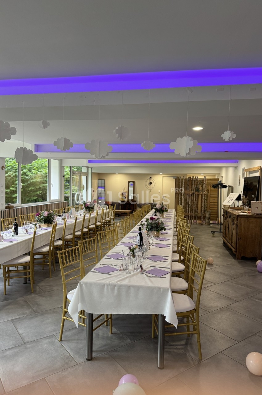 Salle de réception décorée avec de longues tables dressées, des chaises dorées et des nuages suspendus au plafond.