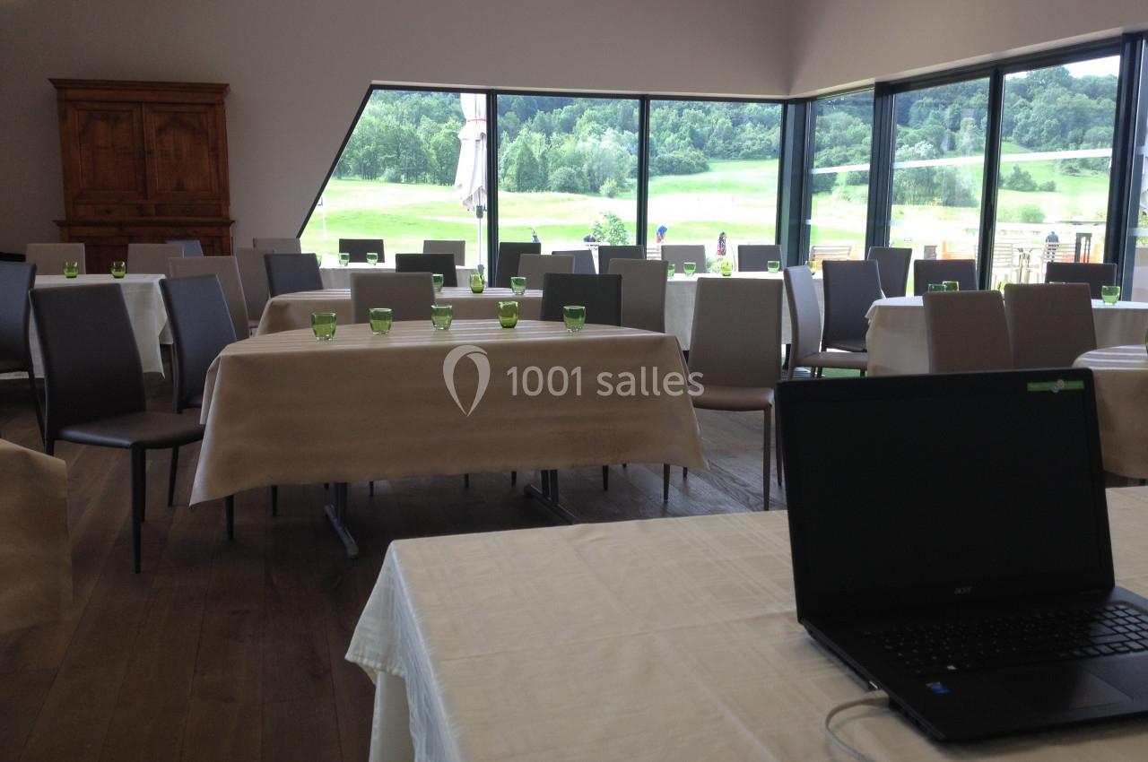 Salle lumineuse avec tables dressées, chaises modernes, grandes baies vitrées donnant sur un paysage verdoyant.