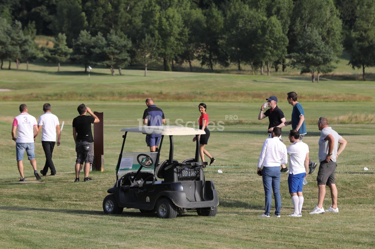 Un groupe de personnes discute près d'une voiturette de golf sur un terrain entouré d'arbres.