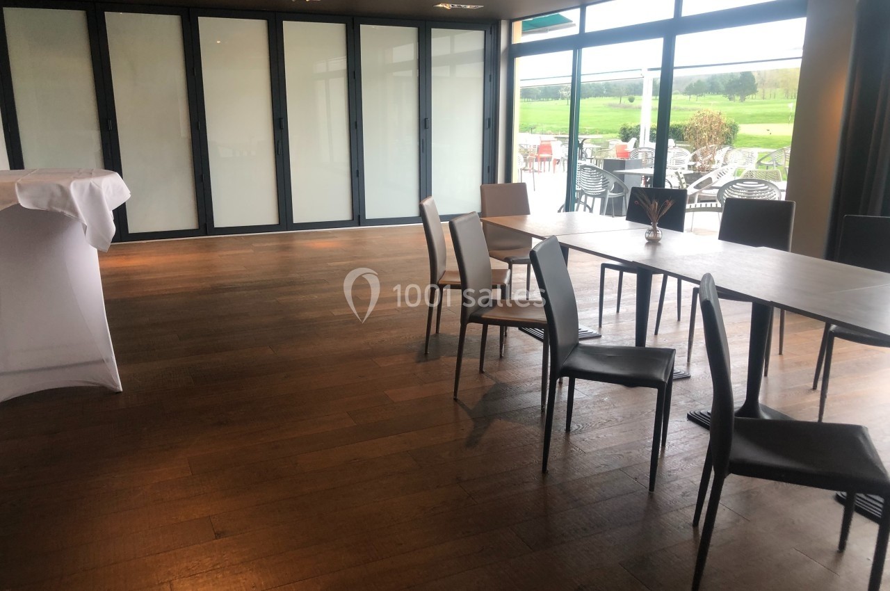 Salle lumineuse avec parquet en bois, tables et chaises modernes, grandes baies vitrées donnant sur une terrasse et un…
