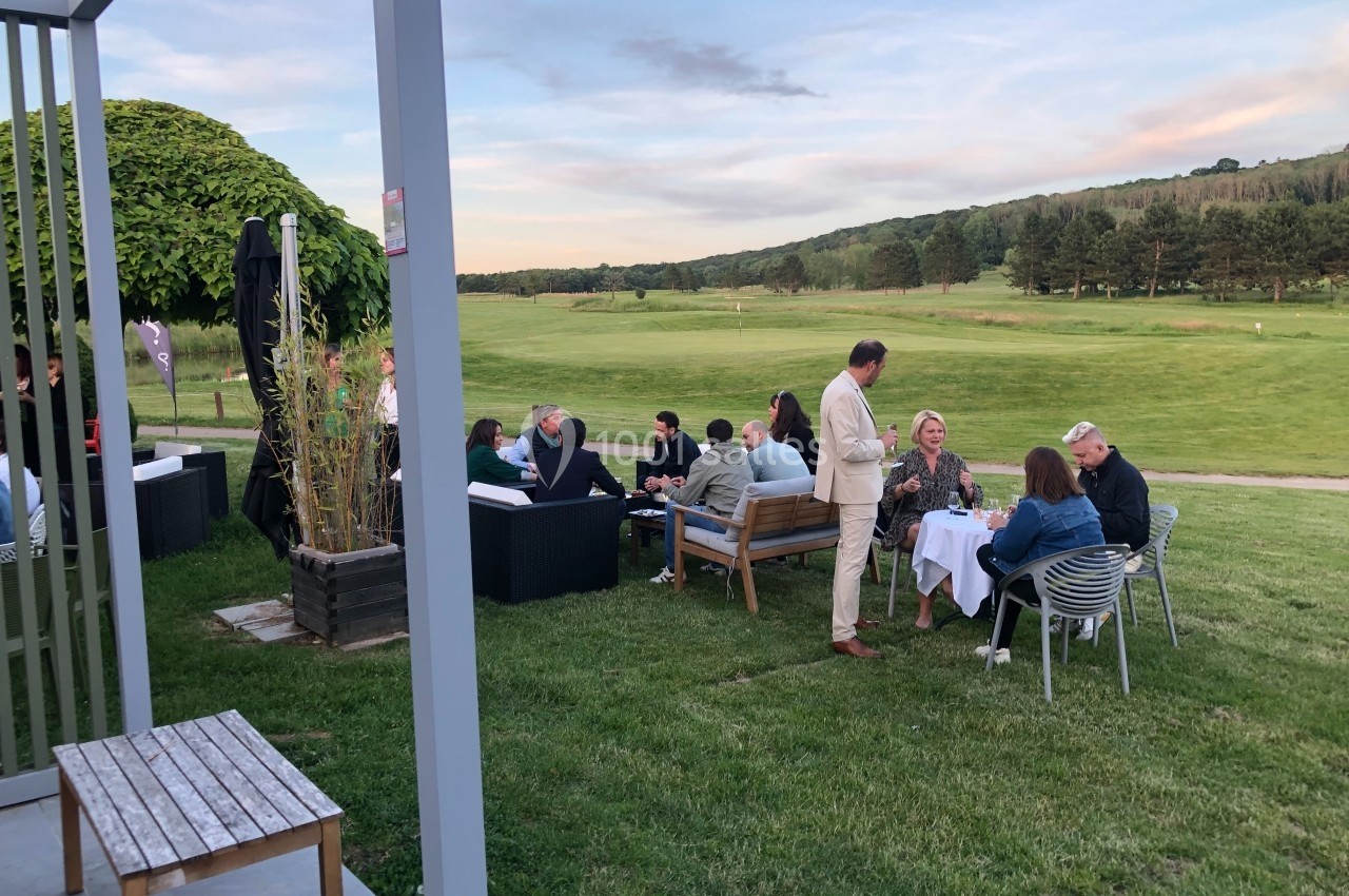Des personnes discutent et dînent en plein air sur une pelouse près d'un terrain de golf, par temps clair.