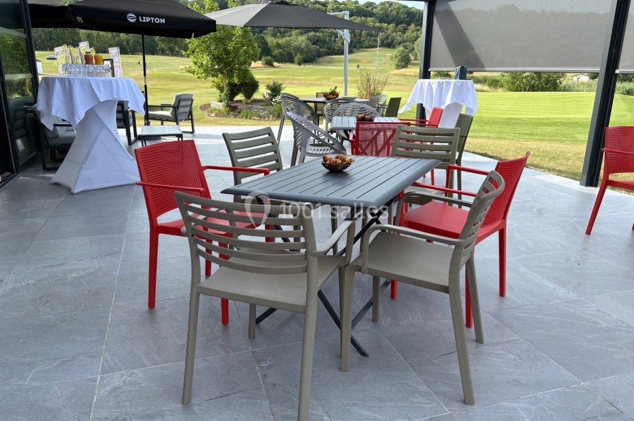 Terrasse avec table et chaises colorées, vue sur un jardin et un terrain verdoyant en arrière-plan.