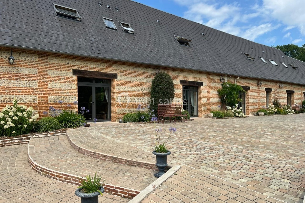 Façade en briques d'un bâtiment avec toit en ardoise, entourée de plantes et donnant sur une cour pavée.