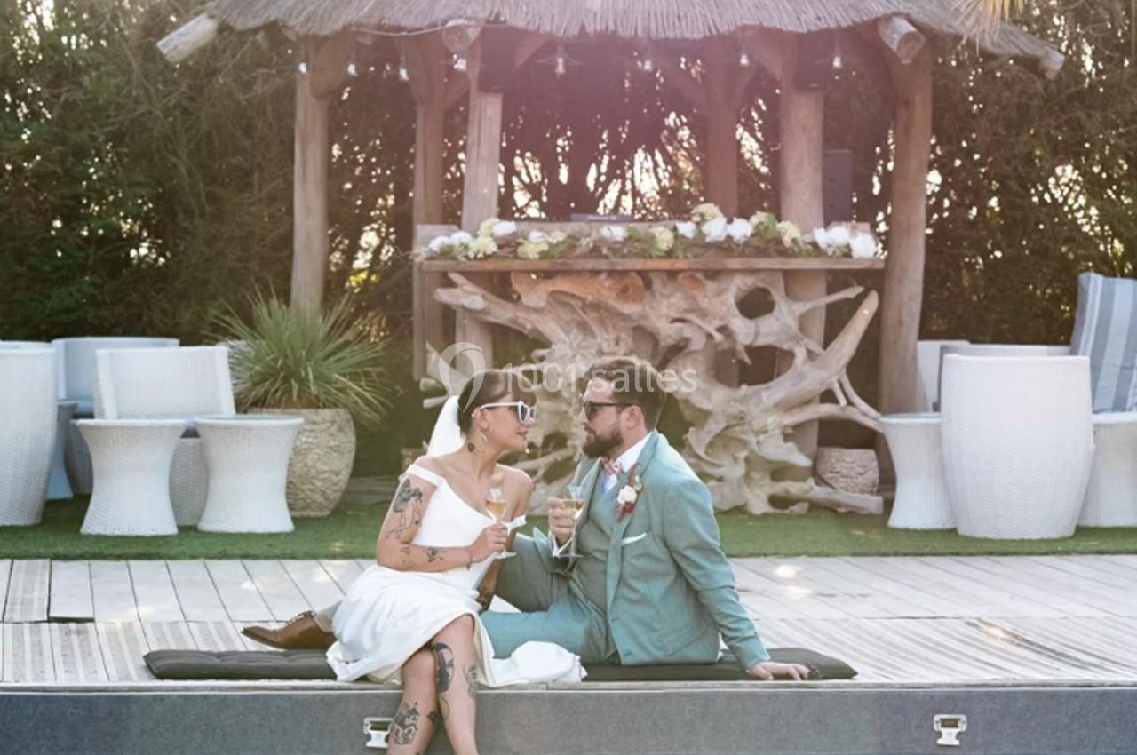 Un couple assis au bord d'une piscine, vêtu élégamment, partage un moment devant un kiosque décoré.